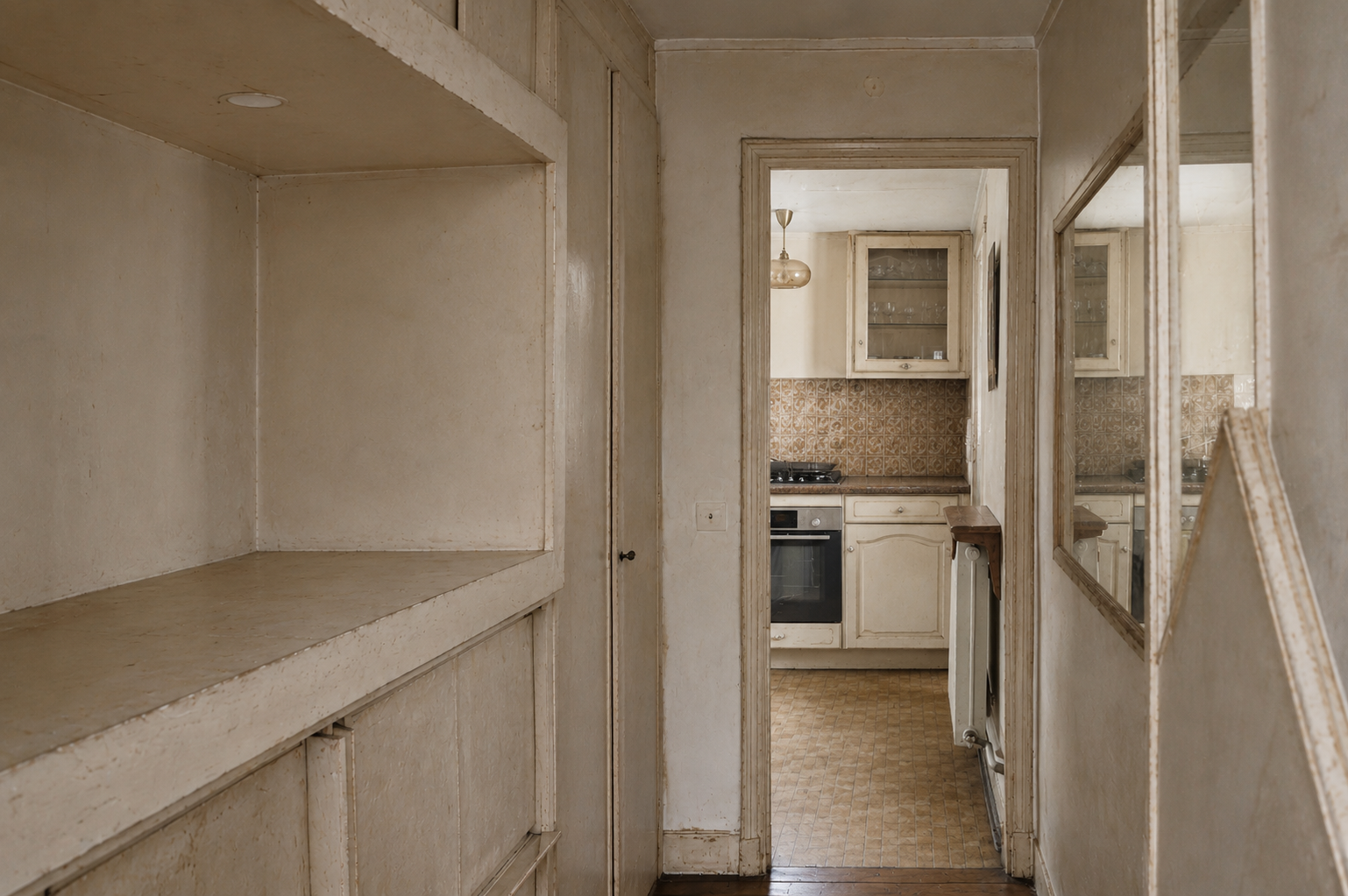 Couloir et cuisine fermée avant rénovation, étagères en bois brut et carrelage vieillot au sol.