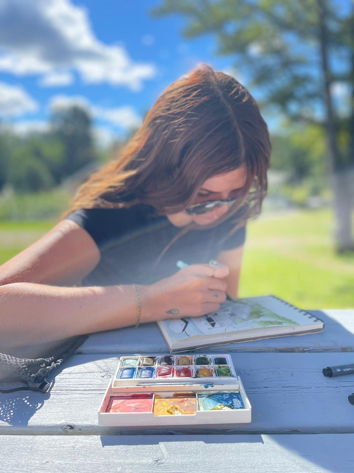 Une architecte utilise des aquarelles pour dessiner en plein air, avec un ciel bleu et des nuages en arrière-plan.