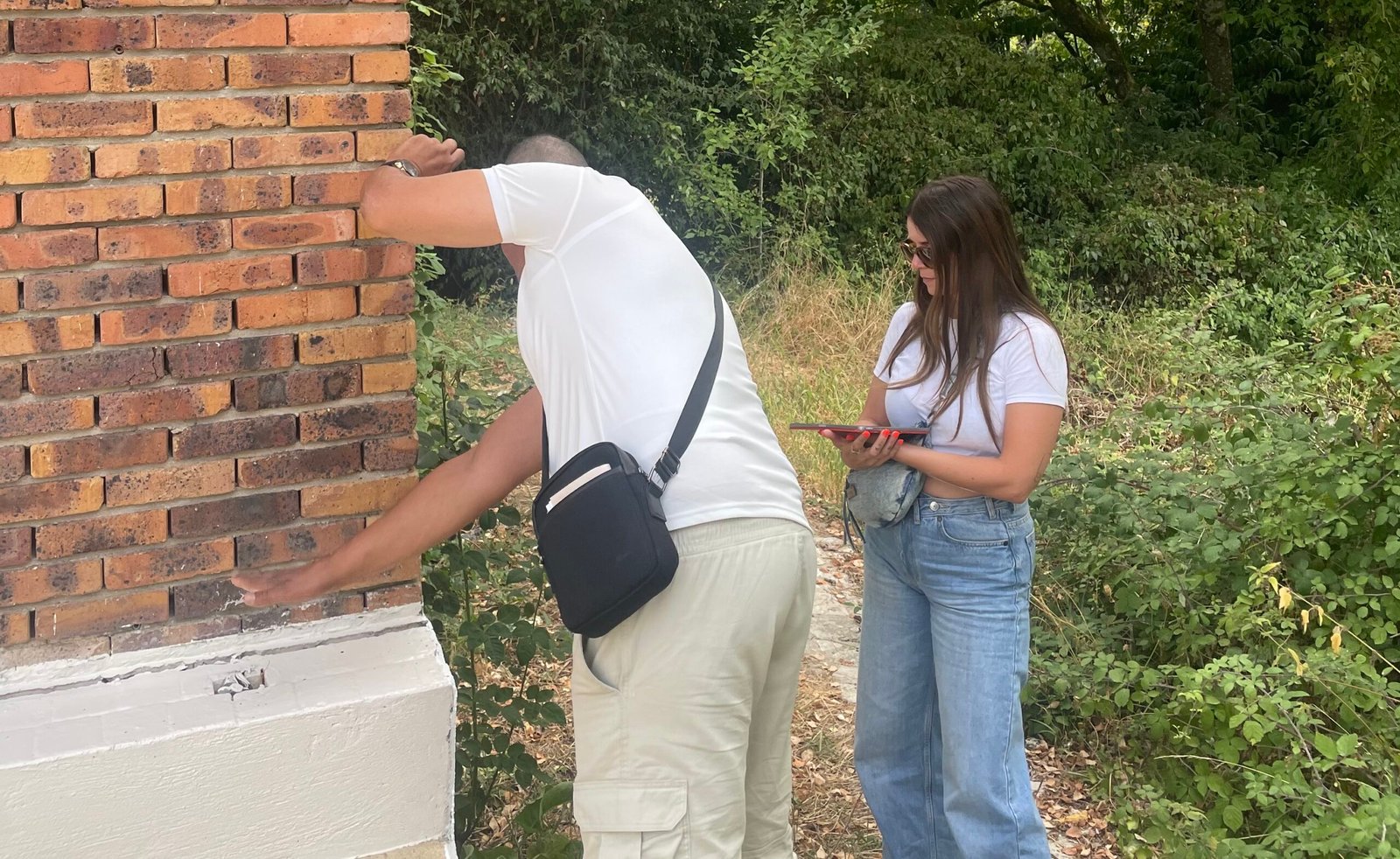 Un ouvrier montre un mur en briques à l'extérieur d'une maison tandis que architecte vérifie le travail réalisé.