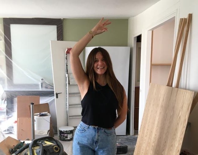 Architecte souriante sur un chantier dans une pièce en rénovation avec des matériaux de construction autour.