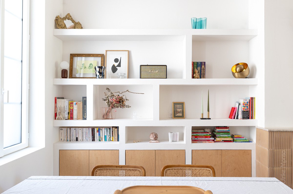 Étagères blanches décorées avec des livres, des objets d'art et des plantes, créant une ambiance moderne et accueillante.