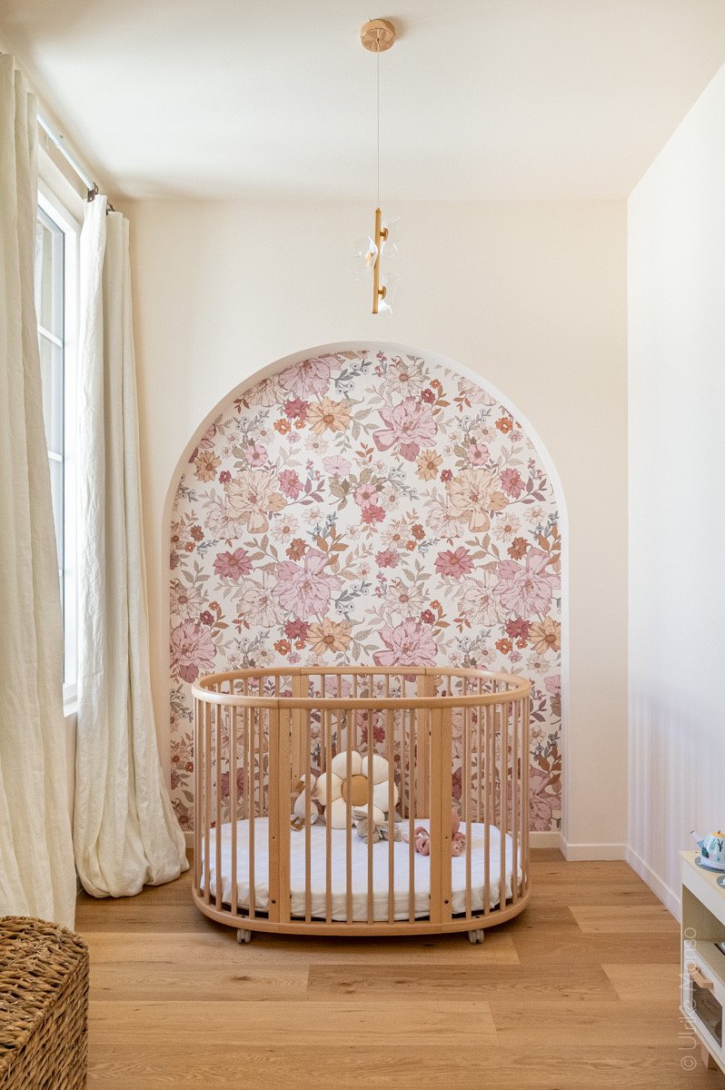 Chambre d'enfant avec un berceau en bois, un mur fleuri et un éclairage moderne, créant une ambiance douce et accueillante.