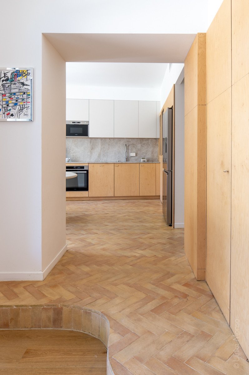 Vue d'un intérieur moderne avec un sol en parquet, une cuisine équipée et des murs clairs.
