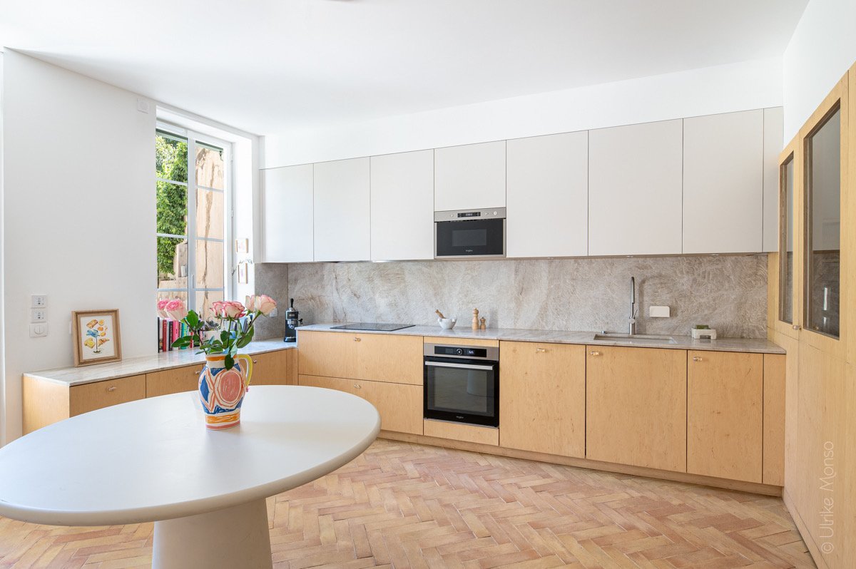 Cuisine moderne lumineuse avec un plan de travail en marbre, des meubles en bois clair et un vase de fleurs sur la table.
