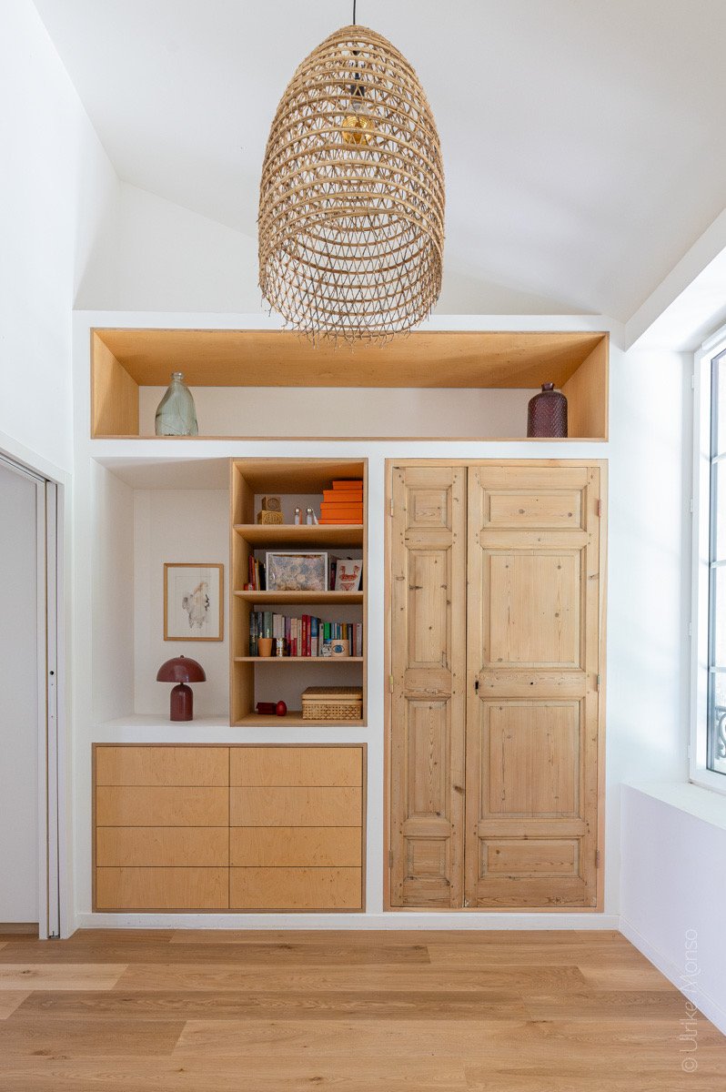 Espace intérieur moderne avec un meuble en bois clair, des étagères et un luminaire en osier suspendu.