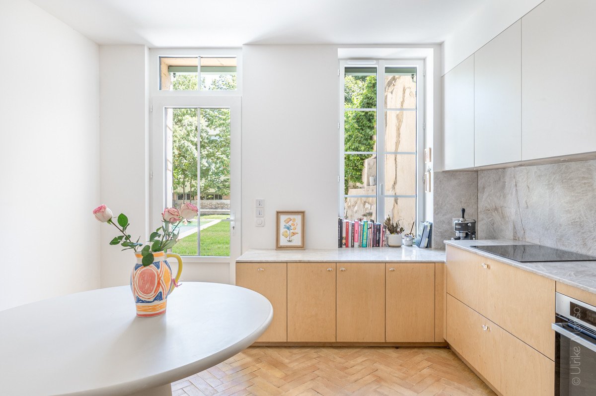 Cuisine moderne lumineuse avec un vase de roses, des fenêtres ouvertes sur un jardin et un mobilier en bois clair.
