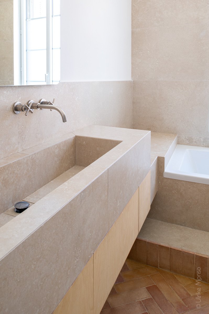 Salle de bain moderne avec lavabo en pierre, miroir et baignoire intégrée, décorée de tons neutres et chaleureux.