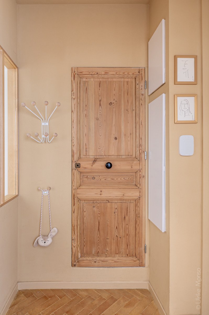 Entrée chaleureuse avec une porte en bois, un porte-manteau moderne et des illustrations encadrées sur un mur beige.