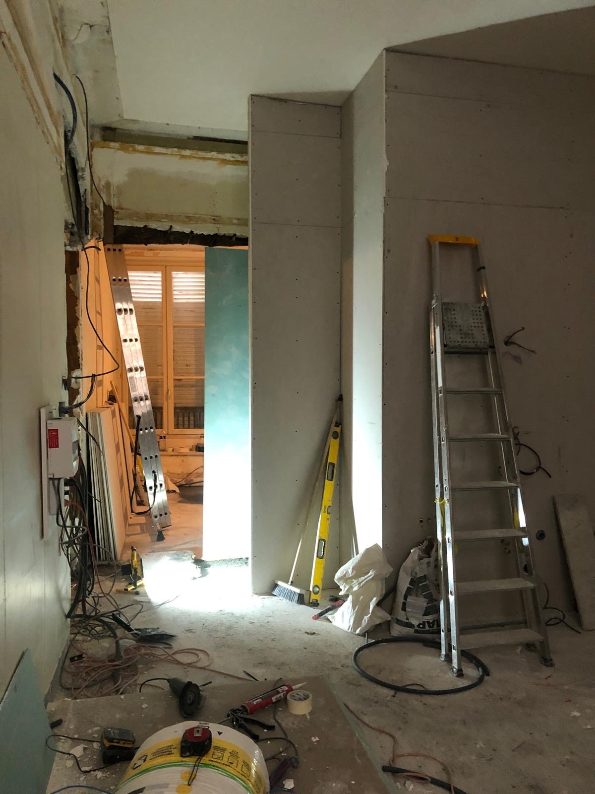 Travaux de rénovation intérieure avec des outils, des matériaux et une échelle dans un espace en cours de transformation.