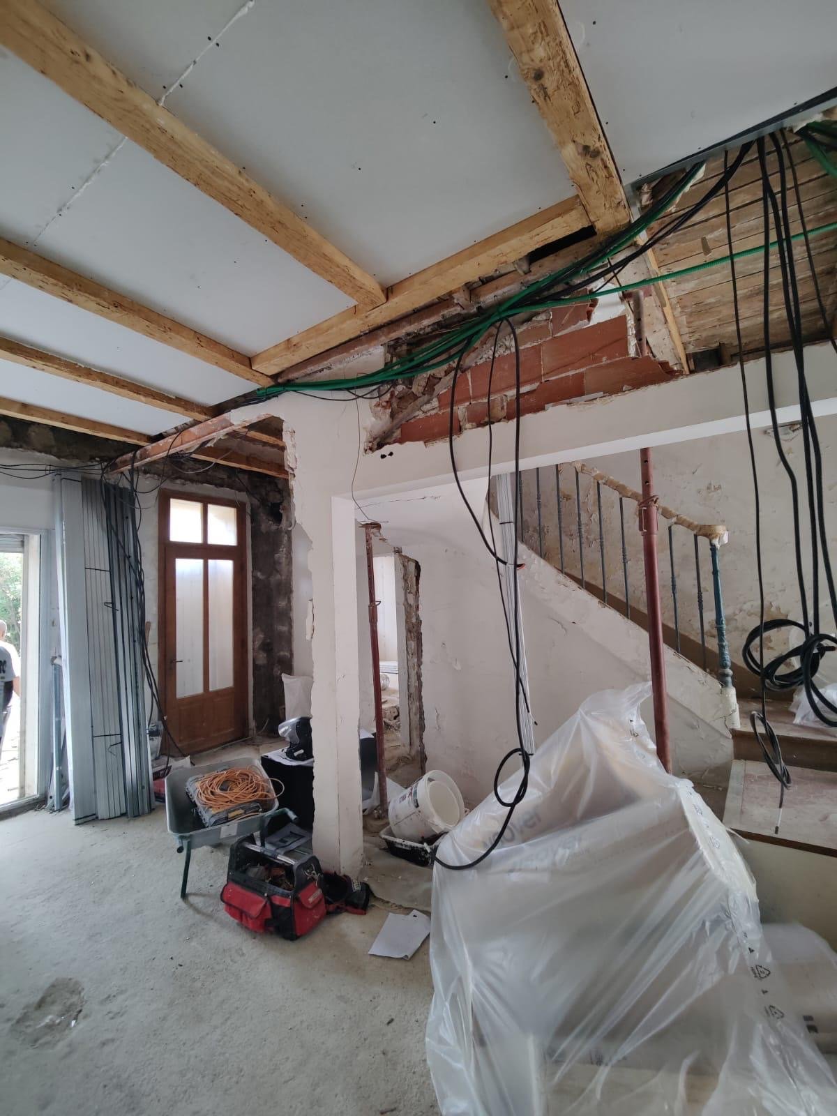 Intérieur d'une maison en rénovation avec câbles électriques, outils et matériaux de construction visibles.